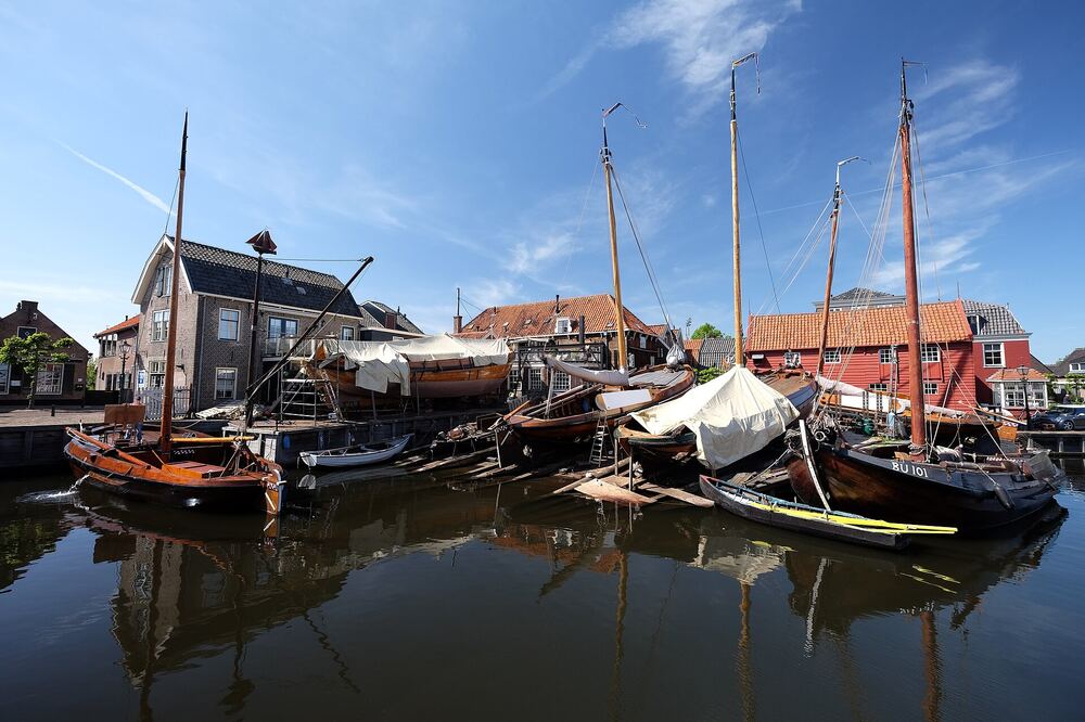 Houten botters met hoge masten liggen afgemeerd in de oude haven van Spakenburg, met historische huizen aan de kade erachter